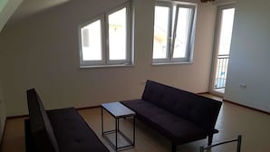 A room with a sofa, a small table, and a chair. There are three windows providing natural light. - Apartmány Horná Seč (Horná Sec)