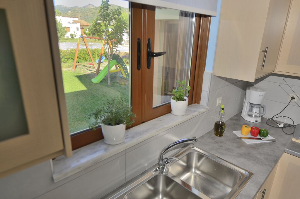 A kitchen with a stainless steel sink, a window with a view of a playground, and a coffee maker on the counter.