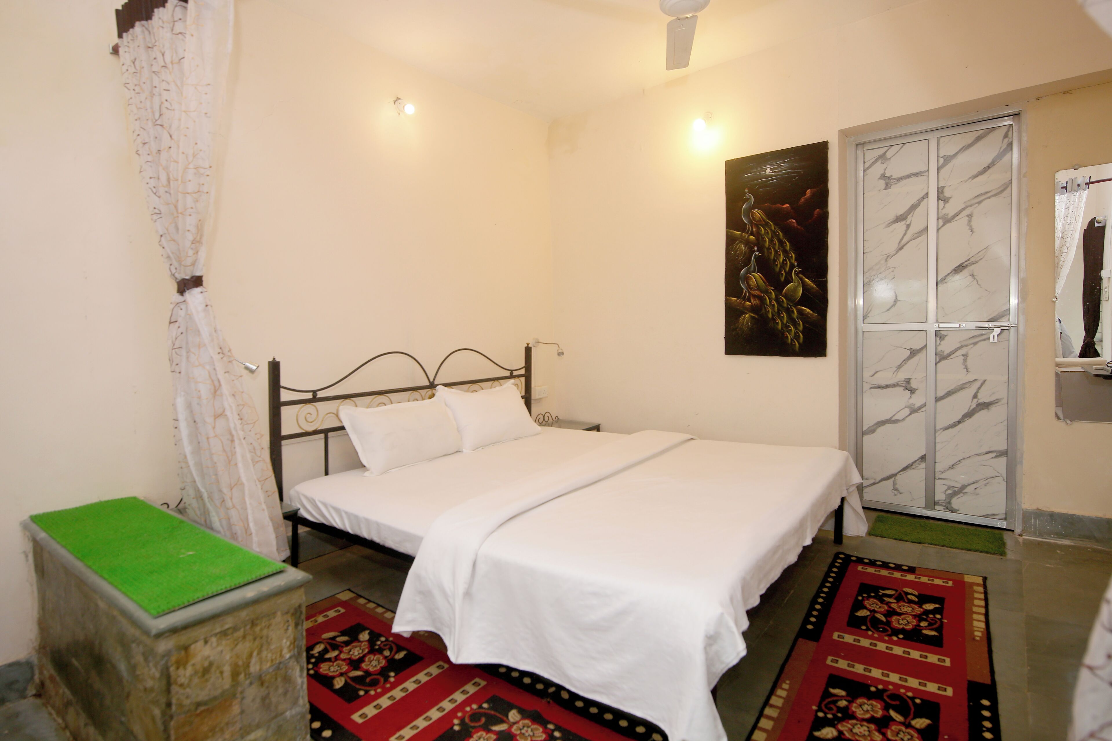 A bedroom with a bed, a green mat, a patterned rug, a marble-framed door, and a painting on the wall.