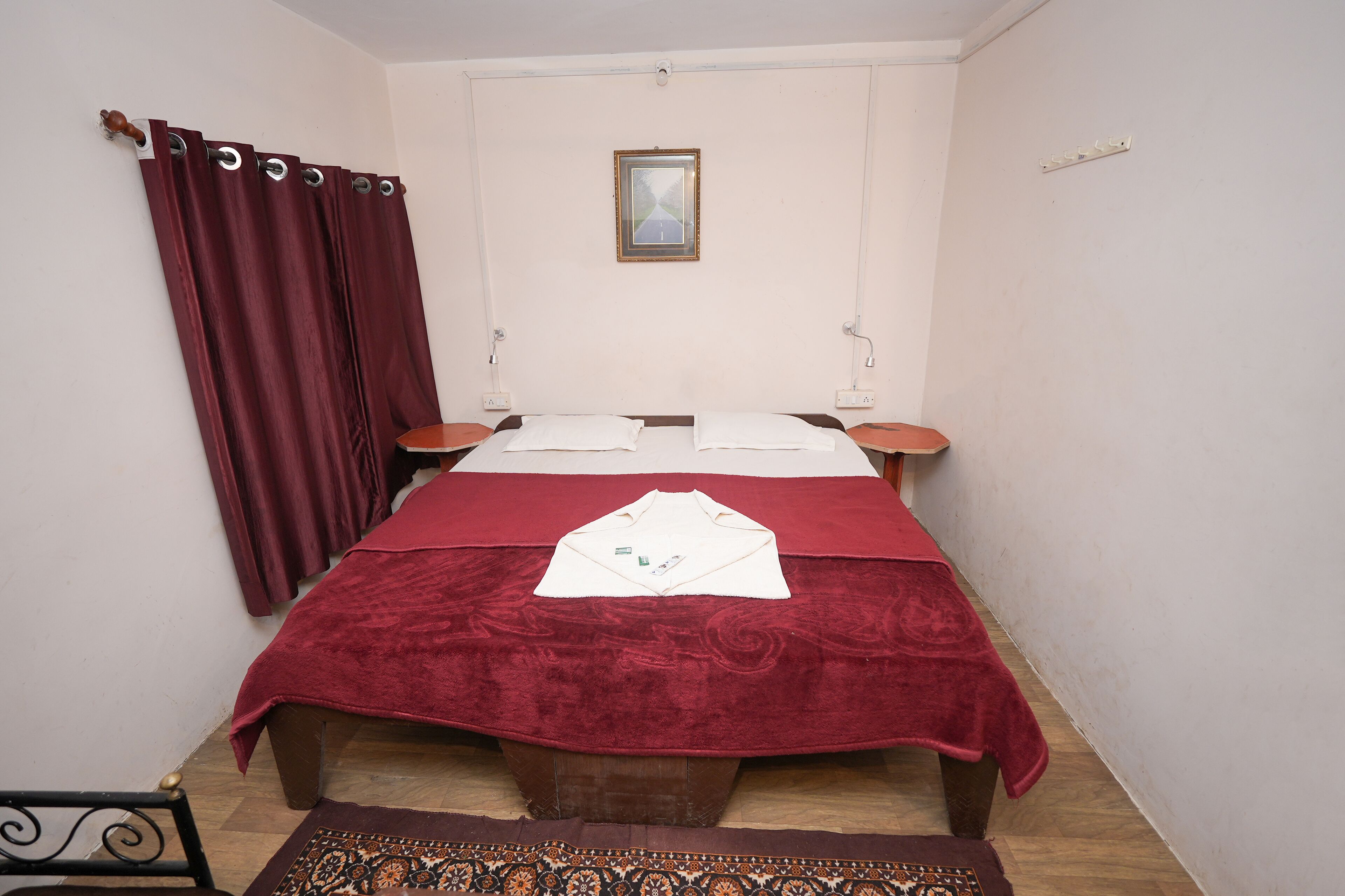 Una cama individual con una colcha roja, un cabecero de madera y una mesita de noche pequeña con una lámpara.