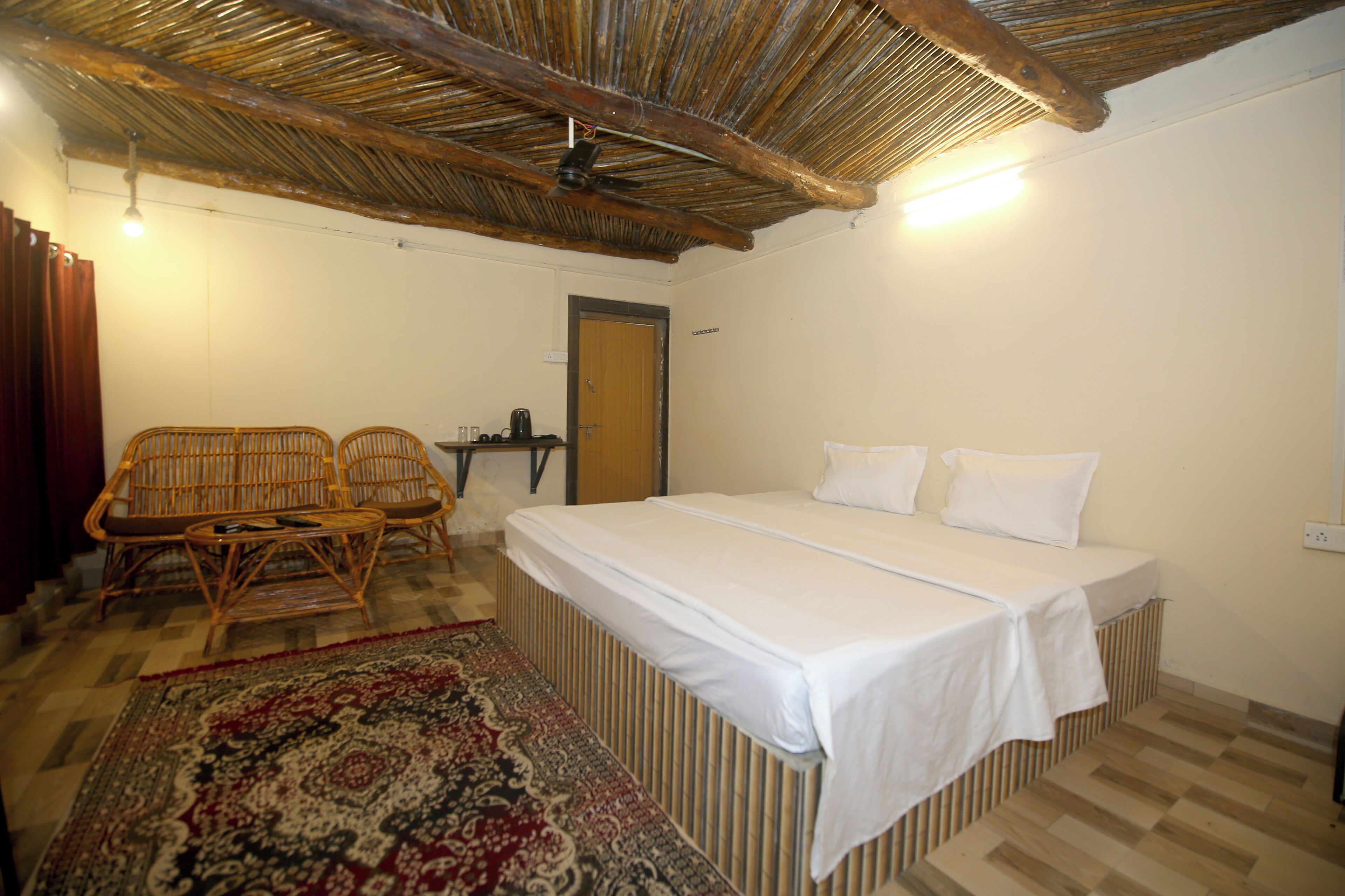 Una habitación con una cama, dos sillas de mimbre, una mesita y una puerta.