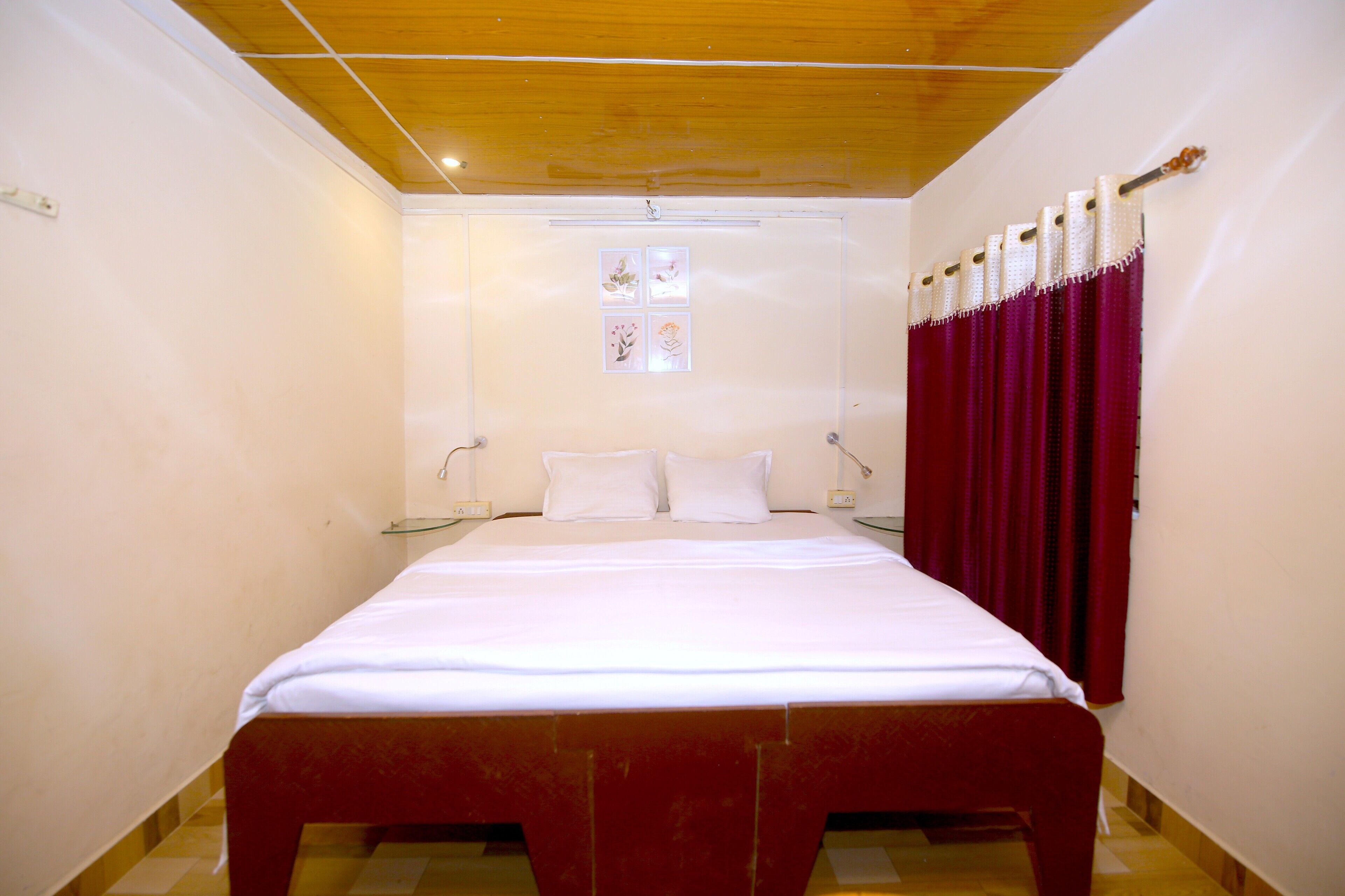 Una camera da letto con soffitto in legno, un letto con biancheria bianca, una finestra con un quadro e tende rosse.