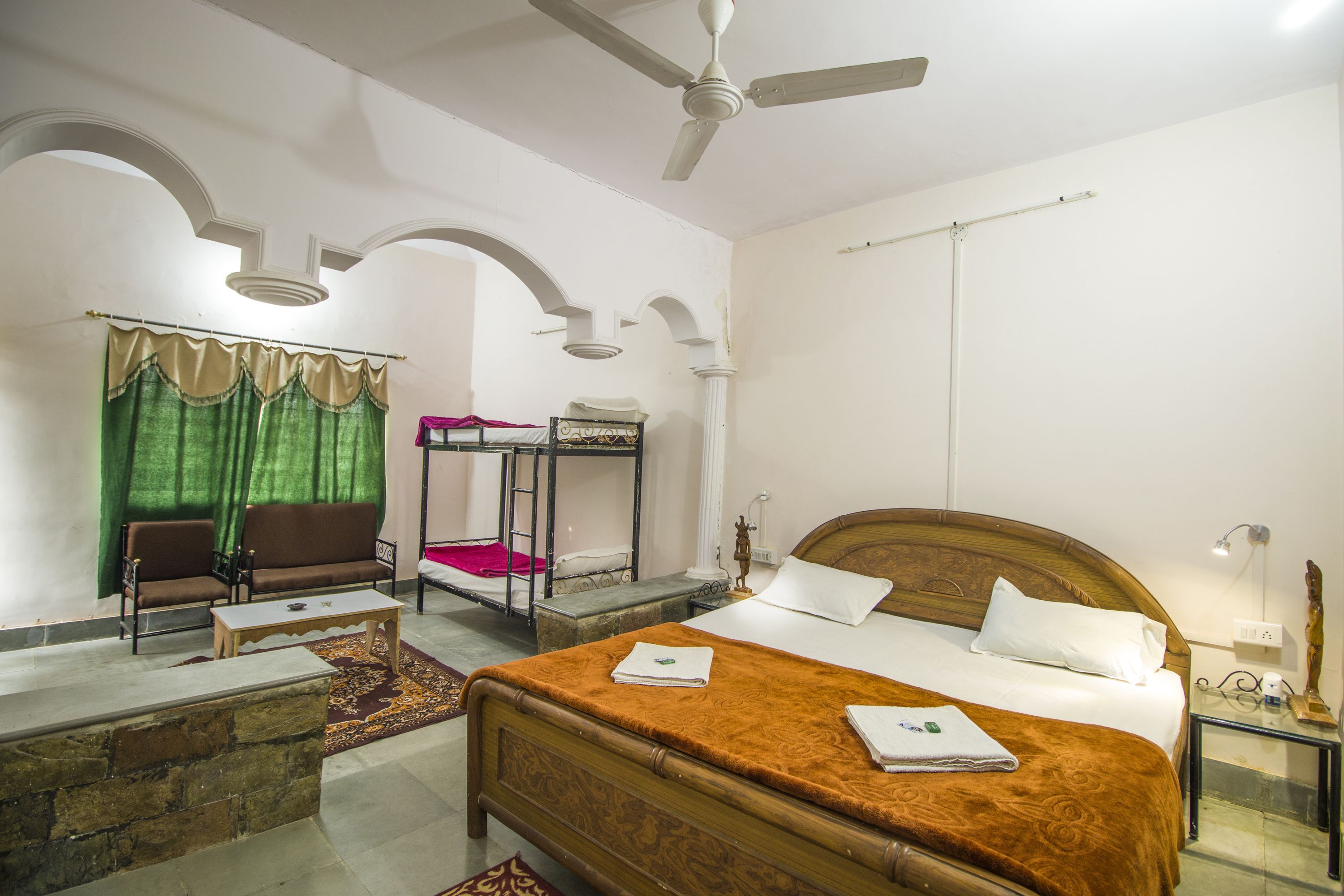 Una habitación de hotel con una cama de madera, un sofá, una mesita, un espejo y un ventilador de techo.
