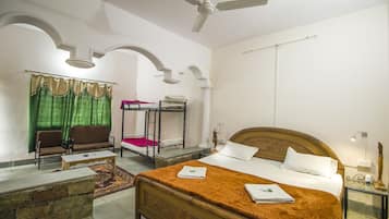 Una habitación de hotel con una cama de madera, un sofá, una mesita, un espejo y un ventilador de techo.
