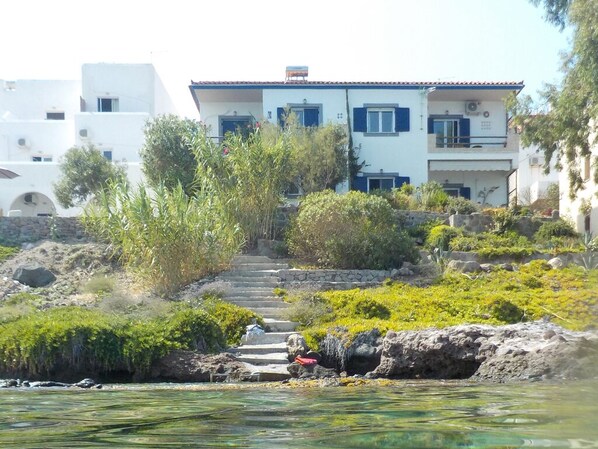 Ein Küstenhaus mit einer Steinstufen-Treppe, die zu einem Balkon führt, umgeben von Grünpflanzen und mit freiem Blick auf das Meer.