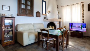 A living room with a sofa, a glass-top dining table, wooden chairs, a television, a fireplace, and a decorative mirror. - Villa Fea - Beach Front Secluded luxury residence with spectacular sea views (Πέρδικα)