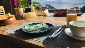 Une table de petit-déjeuner avec un bol de fruits, une assiette de beurre, un verre de jus et divers condiments.