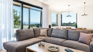 Un salon moderne doté d’un grand canapé d’angle, d’une table basse et offrant une vue sur la ville grâce à de grandes fenêtres.