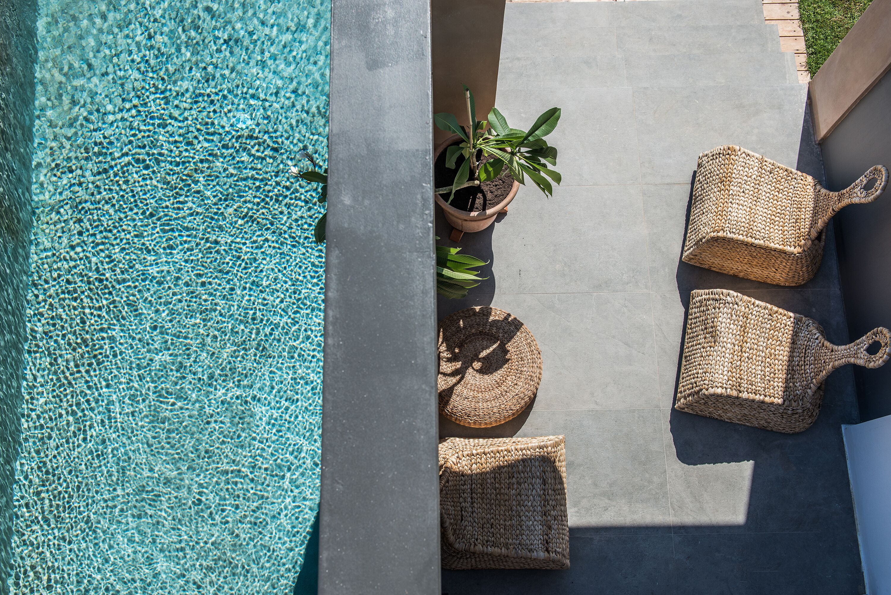 A pool area with clear water, a potted plant, and woven seating.
