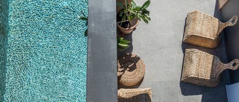 A pool area with clear water, a potted plant, and woven seating.