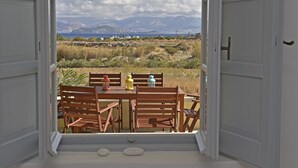 En åben dør fører ud til en balkon med bord og stole, med udsigt over et landskab med bjerge og vand.