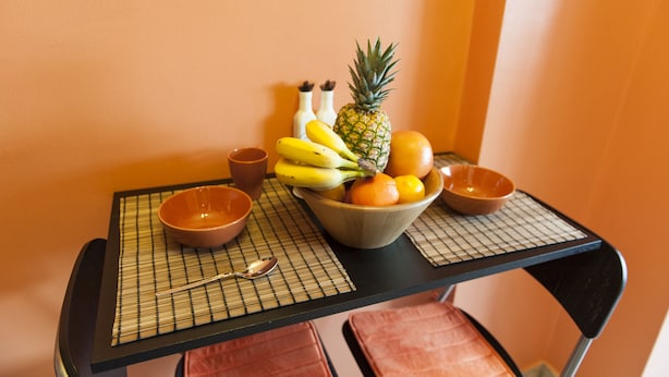 A table with a bowl of fruit, a spoon, and two small bowls on a black table with a grid mat.