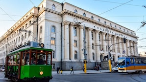 A green tram with the number 35 passing by a large, classical building with columns and a statue on the corner.
