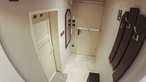 A narrow hallway with a door on the left, a mirror on the right, and a coat rack with hanging items.