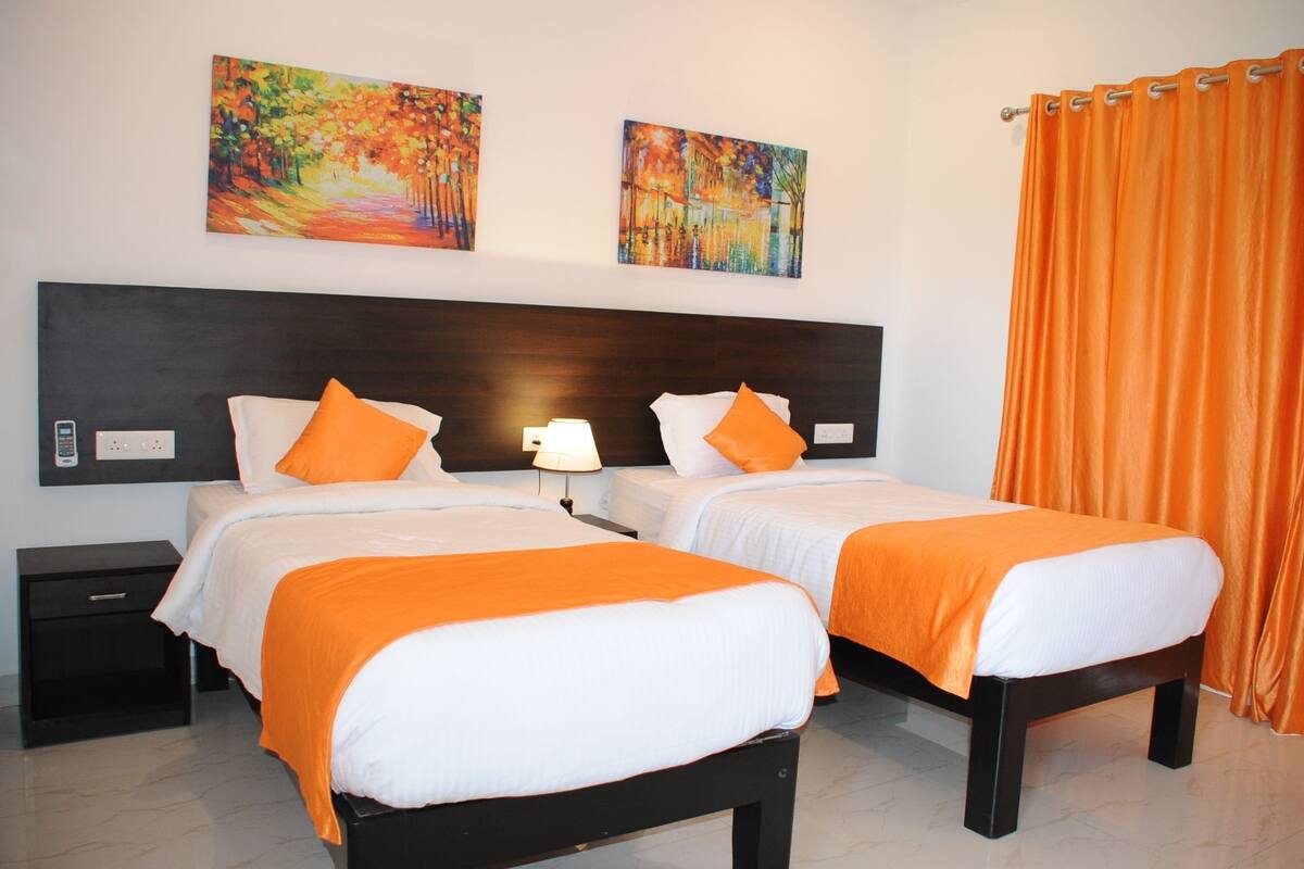 Habitación de hotel con dos camas, una mesita de noche, una lámpara y dos cuadros en la pared.