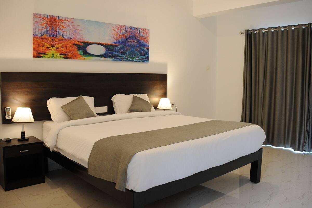 Habitación de hotel moderna con una cama grande, lámparas de noche, una mesita de noche y un cuadro en la pared.