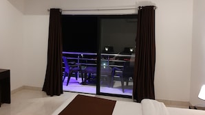 A hotel room with a bed, a desk, a chair, and a balcony with a table and chairs. - JW Heritage (Anjuna)
