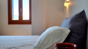 A bedroom with a bed, a window, a wall-mounted light, and a red mug on a table.