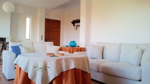 A living room with a white sofa, a table with a tablecloth, and a blue vase.