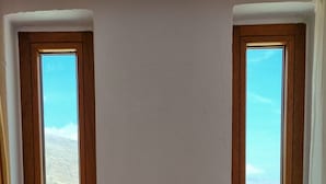 Two windows with wooden frames and white trim, offering a view of a mountainous landscape and a field.