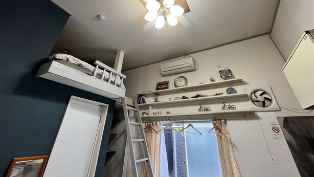 A dormitory room with bunk beds, a ceiling fan, an air conditioner, a window with curtains, and a wall-mounted shelf with various items. - Home WIFI & Compact & Tranquil Apt with LOFT! (杉並区)