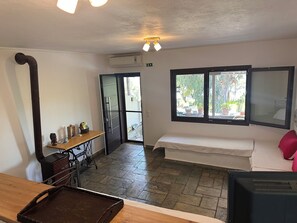 A room with a bed, a desk with a sewing machine, a window with a view of the outdoors, and an air conditioning unit.