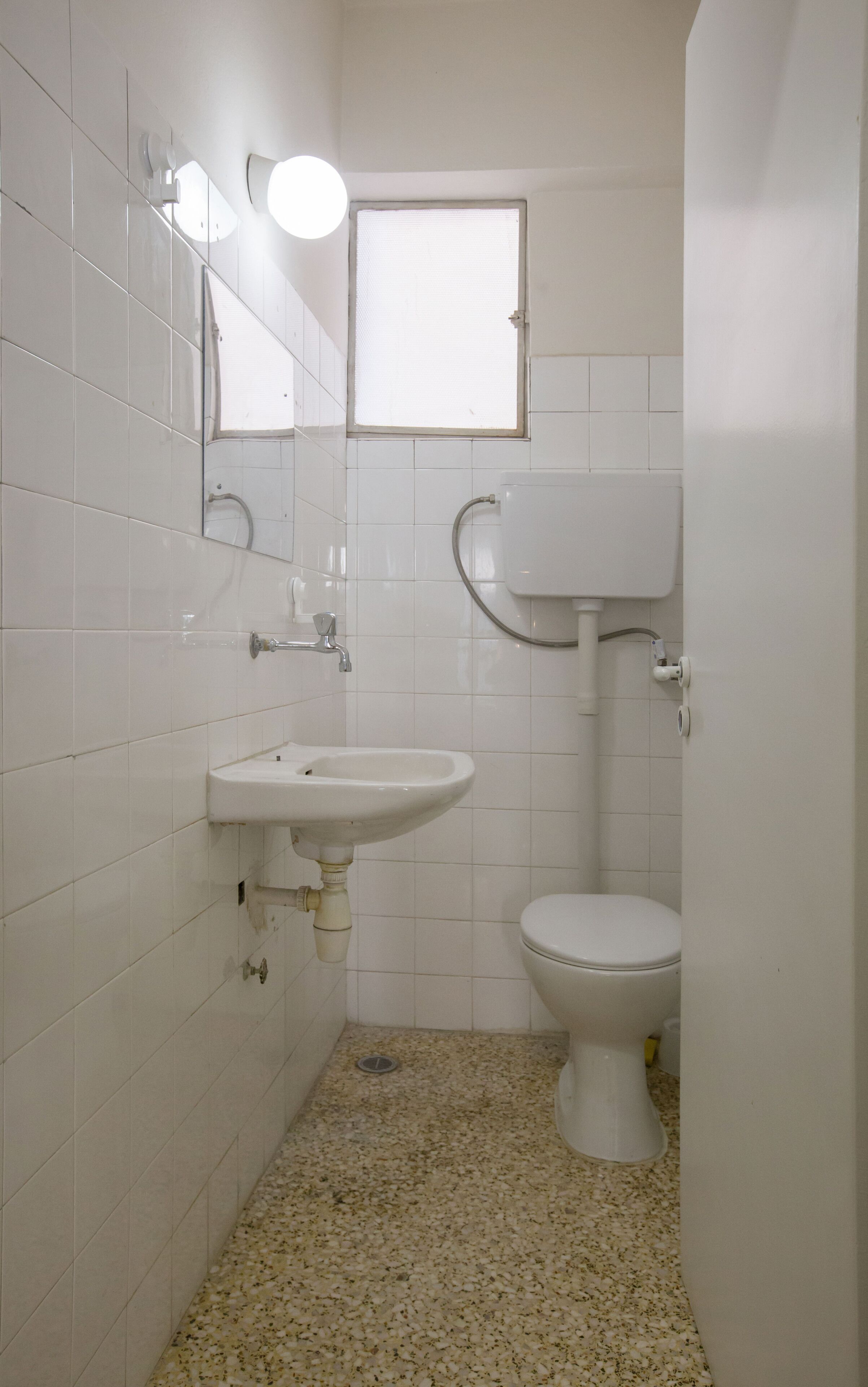 A small, white bathroom with a sink, toilet, and a window.