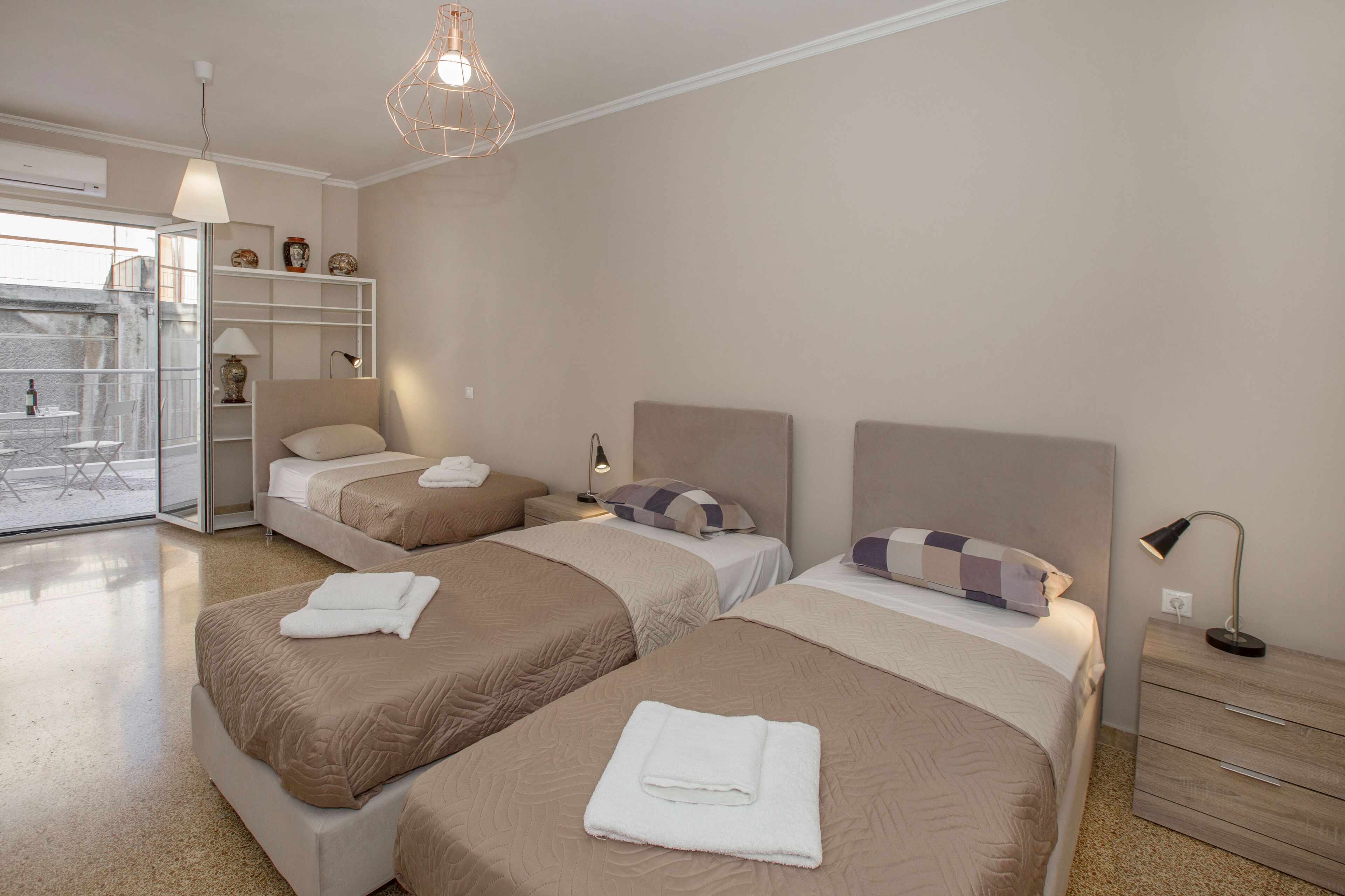 A hotel room with two beds, a glass door leading to a balcony, a bedside table with a lamp, and a wardrobe.