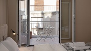 A hotel room with a bed, a desk with a chair, a balcony with a table and chair, and a sliding glass door. - Leonidas Loft in the Heart of Athens by GHH (Athens)