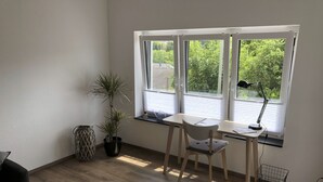 Ein Zimmer mit Schreibtisch, Stuhl, Topfpflanzen und einem Fenster mit Jalousien.
