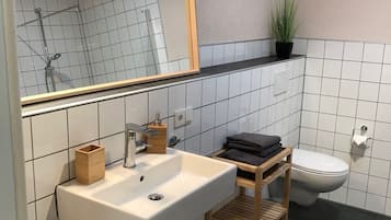 A modern bathroom with a white sink, a mirror, a shower, and a toilet.