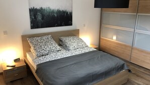 Ein modernes Schlafzimmer mit einem Holzkopfende, einer grauen Bettdecke, gemusterten Kissen, einem Nachttisch mit Lampe und einem Beistelltisch.