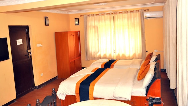A hotel room with two beds, a wooden wardrobe, a door, and a window with curtains. - Kathmadu Fawlty Home (Kathmandu)