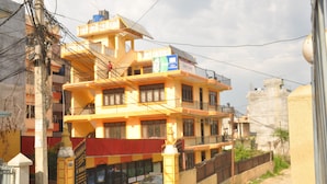 A multi-story building with a yellow facade, a gated entrance, and a parked car in front. - Kathmadu Fawlty Home (Kathmandu)