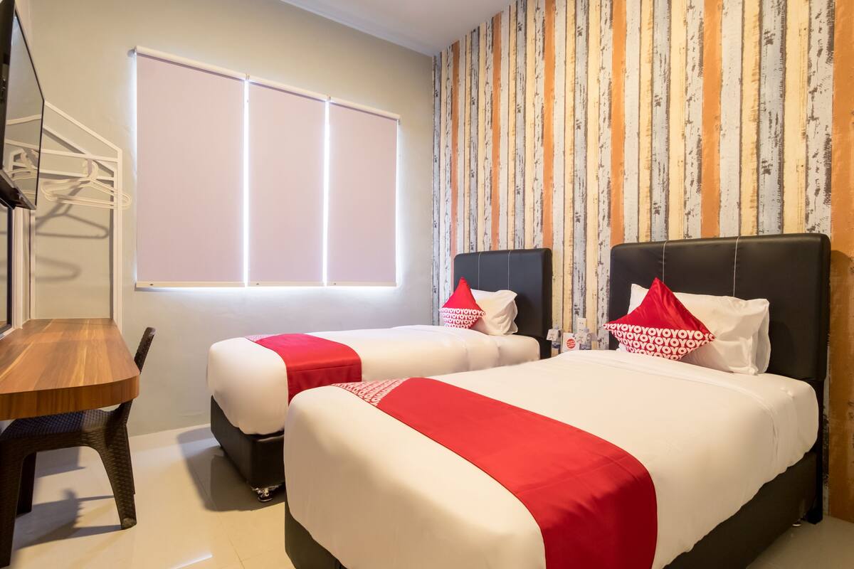 A hotel room with two beds, a wooden table, and a window.