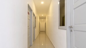 Un long couloir étroit, avec des portes blanches de chaque côté, qui mène à une pièce au bout.