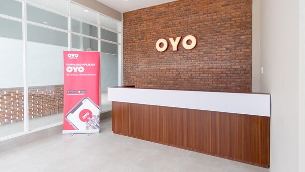 Un comptoir d’accueil avec un revêtement en bois et un mur en briques en arrière-plan. Un grand panneau indiquant le nom de l’hôtel, « OYO », est placé au-dessus du comptoir.