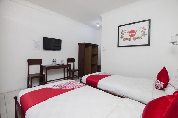 Une chambre d’hôtel avec deux lits, un bureau, une chaise, un téléviseur et un tableau encadré au mur.