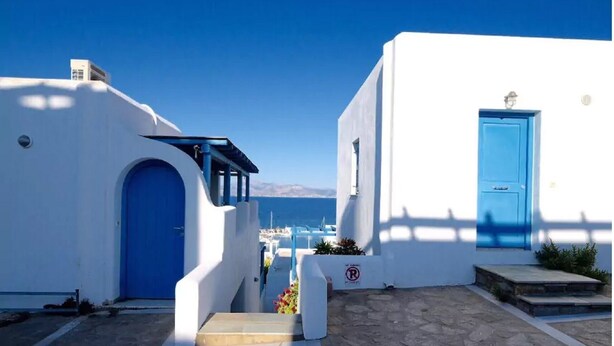 Un bâtiment blanc avec une porte bleue et un escalier bleu menant à une terrasse d’où l’on a une vue sur la mer.