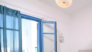 Une pièce dotée d’une grande fenêtre, d’une porte à cadre bleu et d’un mur blanc sur lequel est accroché un sac.