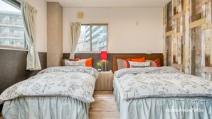 Un dormitorio con dos camas, una ventana con cortinas, una lámpara roja y vistas de edificios.