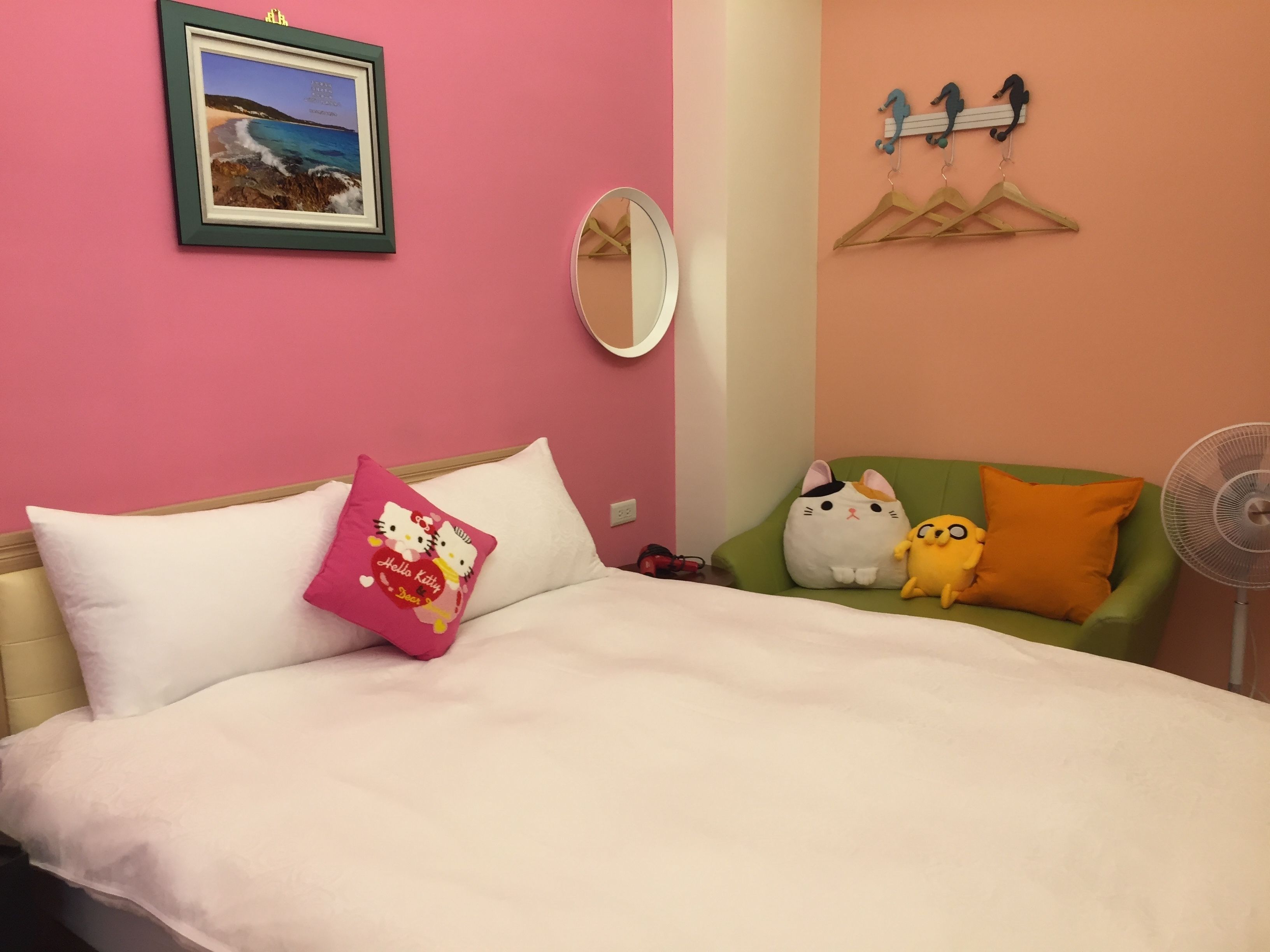 A bedroom with a bed, pillows, a mirror, a wall-mounted fan, and a framed picture.