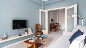 Un salon avec un téléviseur, une table basse, un canapé et, au fond, un coin repas.