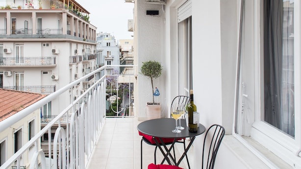 Un balcon avec une table et des chaises, une plante en pot et une fenêtre avec des rideaux.
