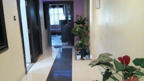 A hallway with a black and white tiled floor, a potted plant on the right, and a door on the left. - Hotel Sai Palace (Bhinmal)