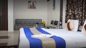A hotel room with a large bed, a sofa, a coffee table, and a chair. - Hotel Sai Palace (Bhinmal)