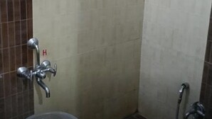 A small, tiled bathroom with a shower, toilet, and a trash bin. - Hotel Sai Palace (Bhinmal)