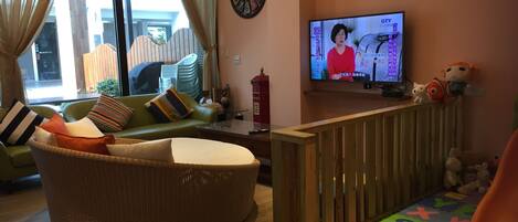 Una sala de estar con un sofá verde, un sillón de mimbre, un televisor y una barandilla de madera.
