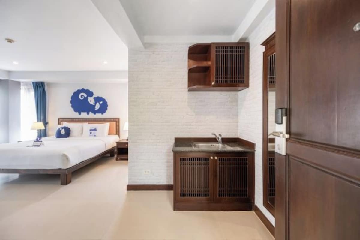Un dormitorio con cama, mesita de noche, estante en la pared y una pequeña kitchenette con lavabo.