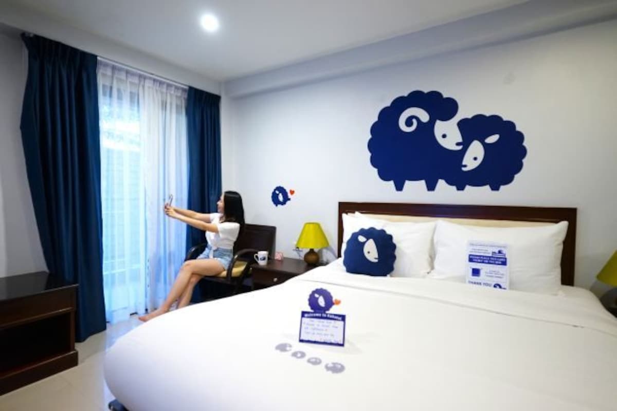 Habitación de hotel con cama, mesita de noche, lámpara y ventana con cortinas.